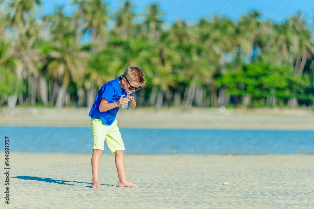 Portrait of a thirsty handsome boy in sunglasses drinking water on the desert tropical beach Portrait of a thirsty handsome boy in sunglasses drinking water on the desert tropical beach