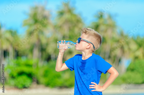 Portrait of a thirsty handsome boy in sunglasses drinking water on the desert tropical beach