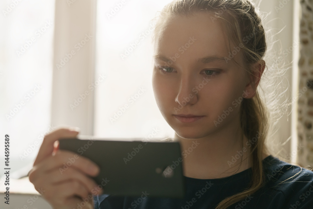 teen girl sitting near window with smartphone, toned photo with shallow focus teen girl sitting near window with smartphone, toned photo with shallow focus