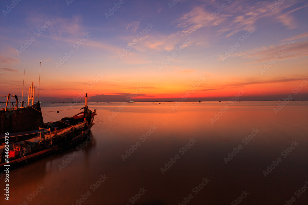 Sunset over sea shore and silhouette shell farm with fishing boat