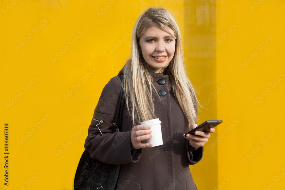 portrait of a smiling Young stylish woman with mobile phone drinking coffee to go in a city street in the morning portrait of a smiling Young stylish woman with mobile phone drinking coffee to go in a city street in the morning