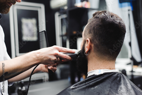 Young handsome barber making haircut of attractive man in barbershop