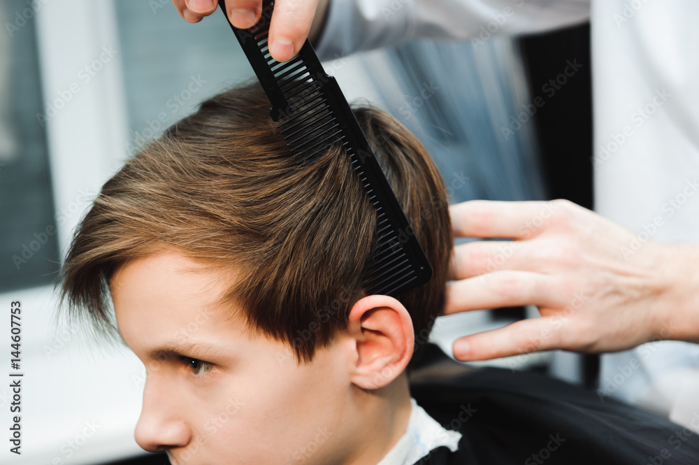 Fototapeta premium Young handsome barber making haircut of cute boy in barbershop