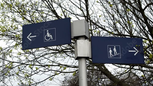 Two signs showing different access directions for able bodied stair access and special needs handicapped ramp access locations.