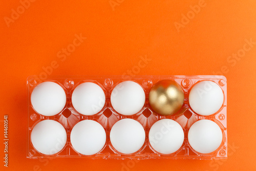 Transparent packaging of chicken eggs with one golden egg on an orange background.