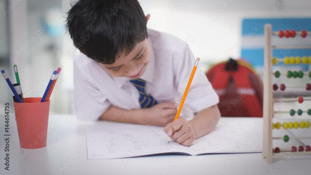 Portrait of happy little boy in classroom writing in exercise book Portrait of happy little boy in classroom writing in exercise book