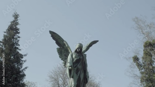 Old tombstone from 20th century with an angel on a sunny spring day. Tilt from sky to angel. 4K in SLOG3. Large shot.