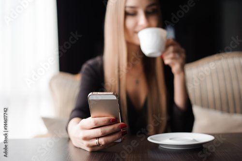 Young woman drinking coffee in a cafe and using a mobile phone
