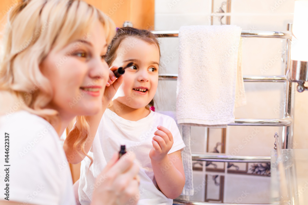 Happy loving family. Mother and daughter are doing makeup and having fun. Mother and daughter sitting at dressing table and looking at the mirror.