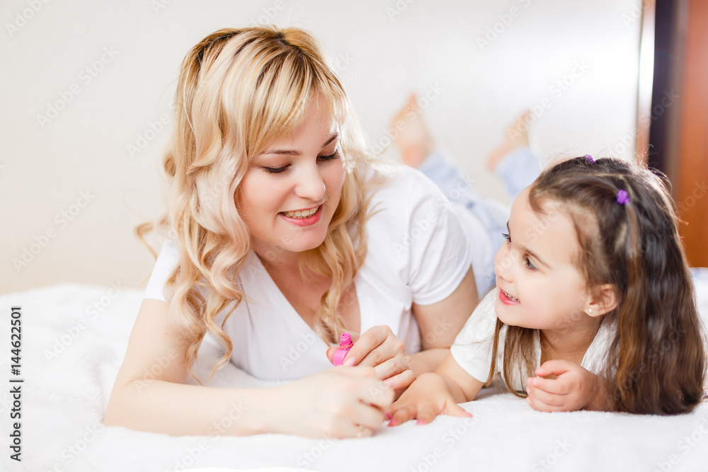 Mom and daughter in the bedroom on the bed in the curlers make up, paint their nails and have fun Mom and daughter in the bedroom on the bed in the curlers make up, paint their nails and have fun