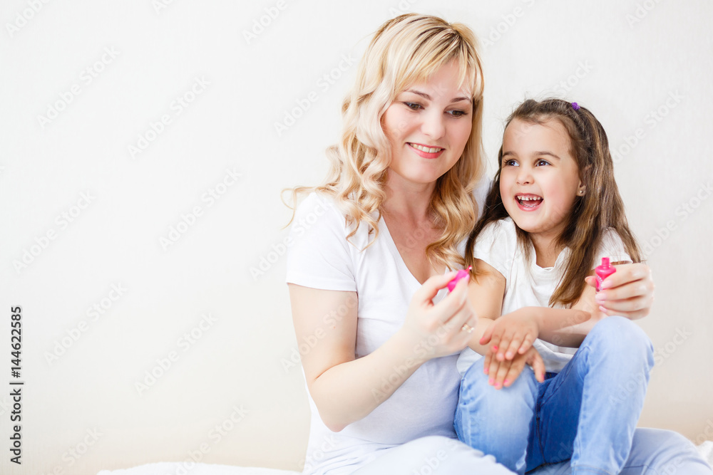 Mom and daughter in the bedroom on the bed in the curlers make up, paint their nails and have fun Mom and daughter in the bedroom on the bed in the curlers make up, paint their nails and have fun