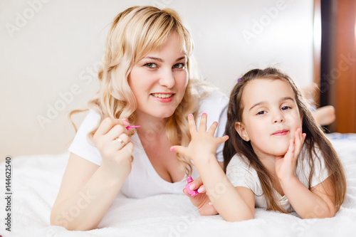 Mom and daughter in the bedroom on the bed in the curlers make up  paint their nails and have fun