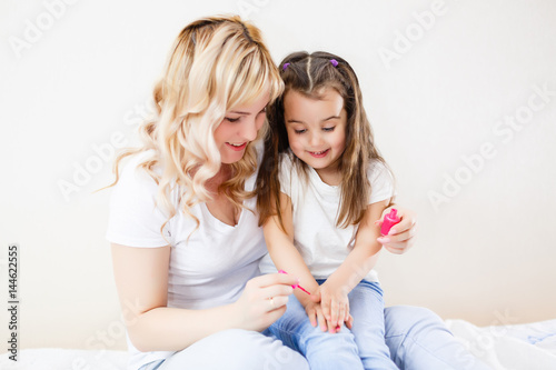 Mom and daughter in the bedroom on the bed in the curlers make up, paint their nails and have fun