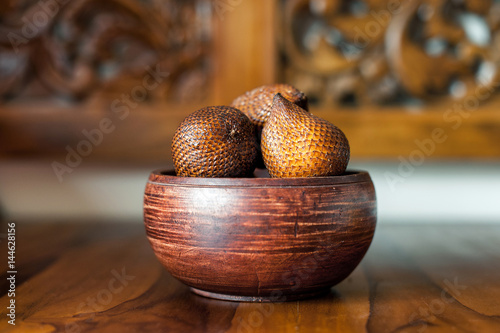 Brown wooden bowl with salak or snake fruits. Carving wooden background. Exotic fruits from Bali, Indonesia photo