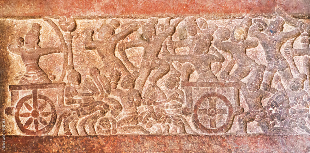 Battle scene with warriors on a four-wheeled wagons, carved wall inside the 7th century temples in Pattadakal, India. UNESCO World Heritage site