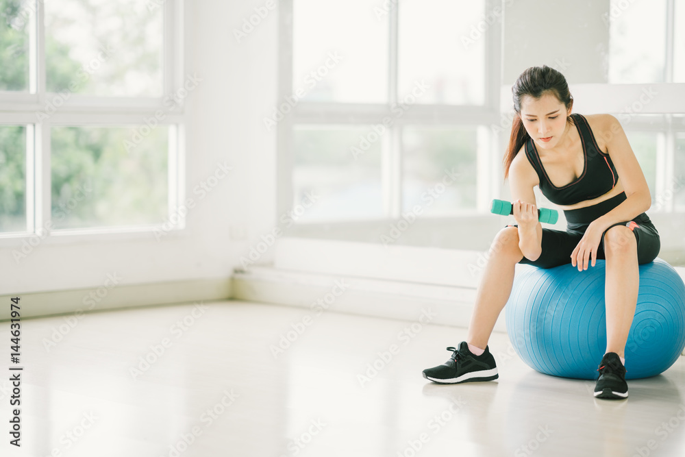 Sexy Asian girl exercising with dumbbell on fitness ball at fitness gym with copy space, sport and healthy lifestyle concept Sexy Asian girl exercising with dumbbell on fitness ball at fitness gym with copy space, sport and healthy lifestyle concept