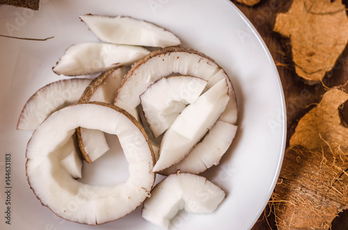 Chopped coconut in a white plate on a wooden background.