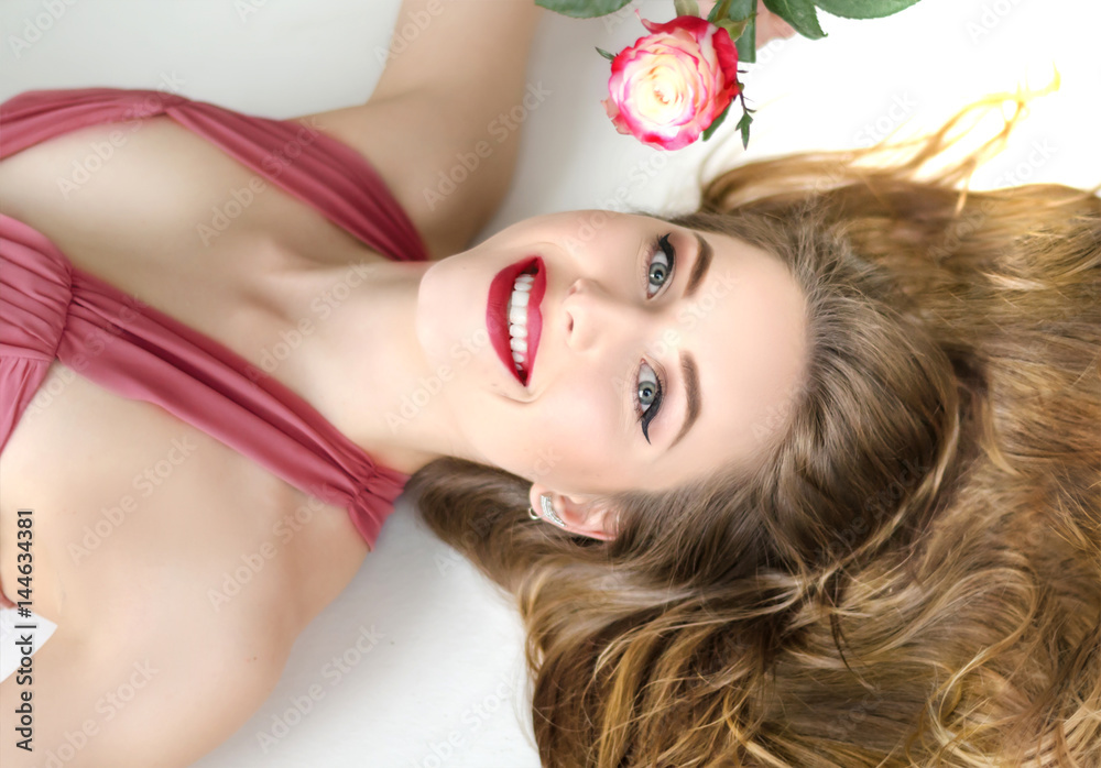 Portrait of young attractive woman lying with rose and long hair, wearing red dress Portrait of young attractive woman lying with rose and long hair, wearing red dress