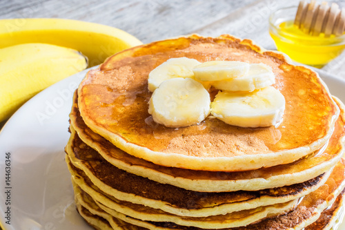 delicious pancakes with banana and honey over rustic wooden table
