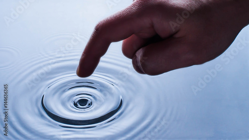 Close up finger touches water and drop of water falling and creating natural and calm waves