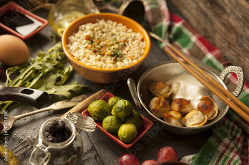 Table with food in breakfast or lunch: omelette, cabbage, oil, chili, ketchup, arugula, onion, garlic, noodles, cucumber, coffee, biscuits, orange, bread and butter