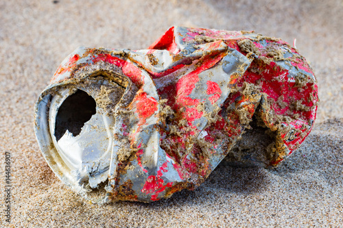bunched up old red tin can lies in the sand on the beach