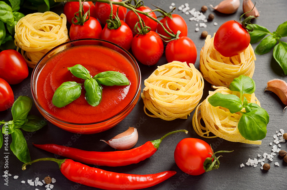 Tomato sauce with pasta and ingredients on black background