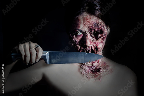  horrible scary zombie girl with a kitchen knife on black background with copyspace