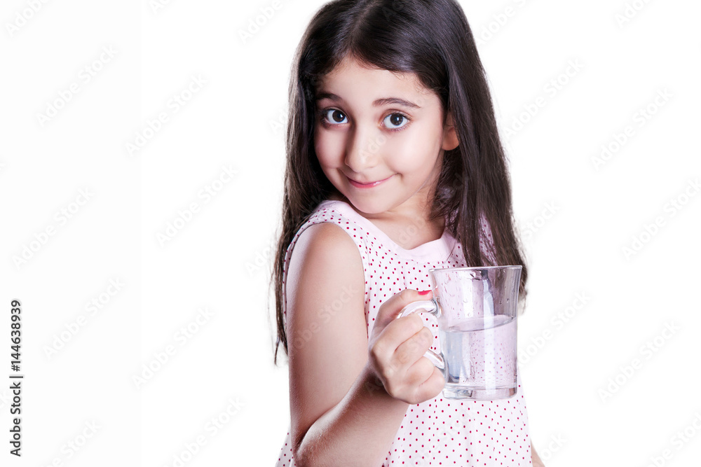 Beautiful happy little girl with long dark hair and dress holding glass of water and looking at camera. studio shot, isolated on white background.. Beautiful happy little girl with long dark hair and dress holding glass of water and looking at camera. studio shot, isolated on white background..