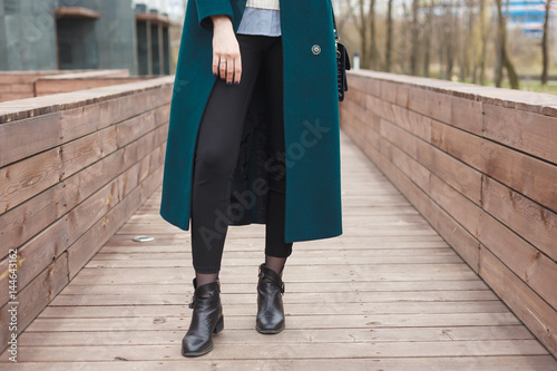 Black ankle boots, black leather bag, warm emerald coat and black trousers. Stylish and fashionable girl on a walk