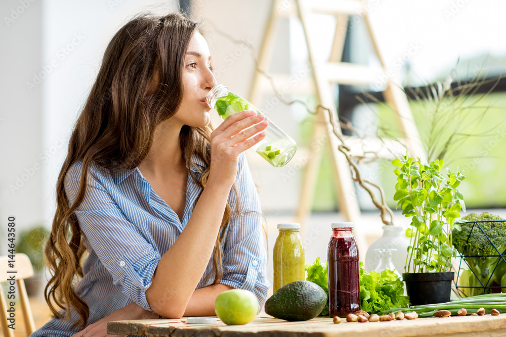 Plakat Piękna kobieta siedzi z napojami i zdrową, zieloną żywnością w domu. Wegański posiłek i koncepcja detoksykacji
