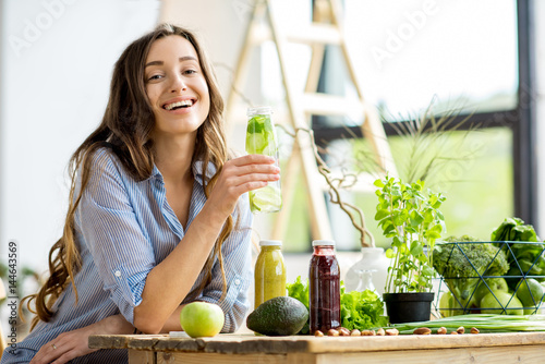 Beautiful happy woman sitting with drinks and healthy green food at home. Vegan meal and detox concept