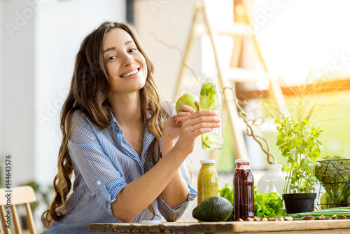 Beautiful happy woman sitting with drinks and healthy green food at home. Vegan meal and detox concept