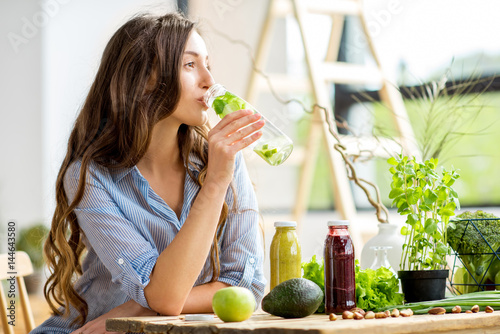 Fototapeta Beautiful woman sitting with drinks and healthy green food at home