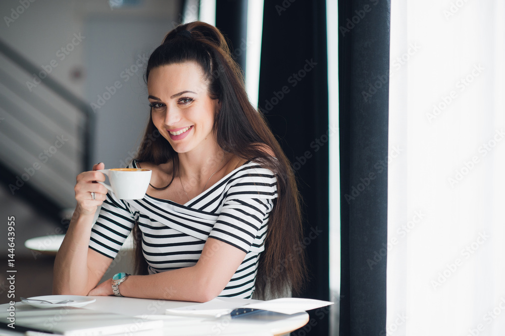 Beautiful adult woman with a perfect smile and white teeth sitting in a cafe near a window and holding a cup of coffee. Beautiful adult woman with a perfect smile and white teeth sitting in a cafe near a window and holding a cup of coffee.