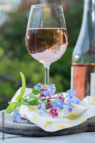 Glass of cold rose wine, outdoor terrace, sunny day, spring garden flowers