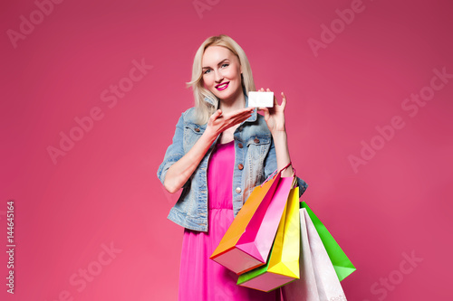 Shopping woman holding shopping bags on pink background . Holds a white nameplate for your text