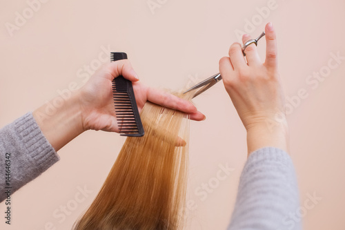 The hairdresser does a haircut with scissors of hair to a young girl, a blonde in a beauty salon.