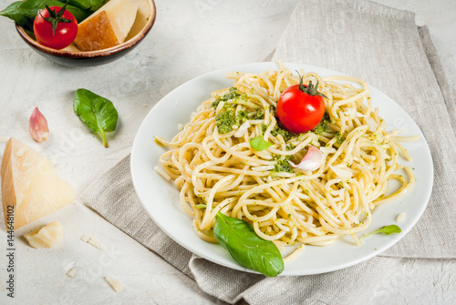 Italian cuisine, lunch or dinner for one. Pesto pasta. Spaghetti with pesto, basil leaves, garlic, parmesan cheese and cherry tomatoes. One portion. On a white stone table. Copy space