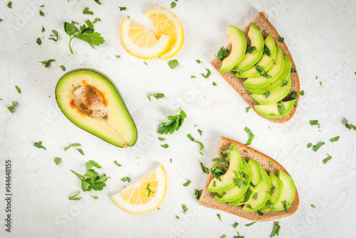 Healthy diet food. Spring meal. Sandwiches of black bread with avocado, lemon and greens. With ingredients on cutting board on white stone table