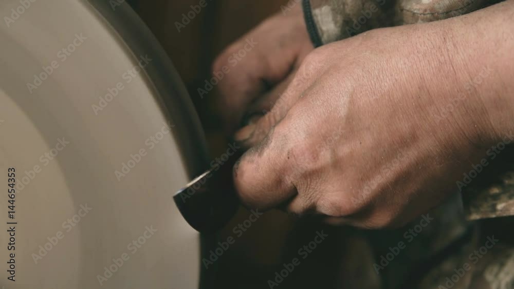 Closeup of hands grinding metal knife at grindstone machine in traditional smithy