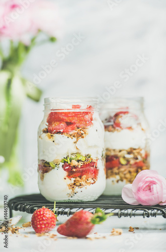 Healthy spring breakfast. Greek yogurt, granola, fresh strawberry breakfast jars, pink raninkulus flowers, marble background, selective focus, copy space. Clean eating, detox vegetarian food concept