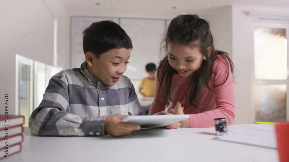 Happy little boy & girl working on computer tablet in school classroom Happy little boy & girl working on computer tablet in school classroom