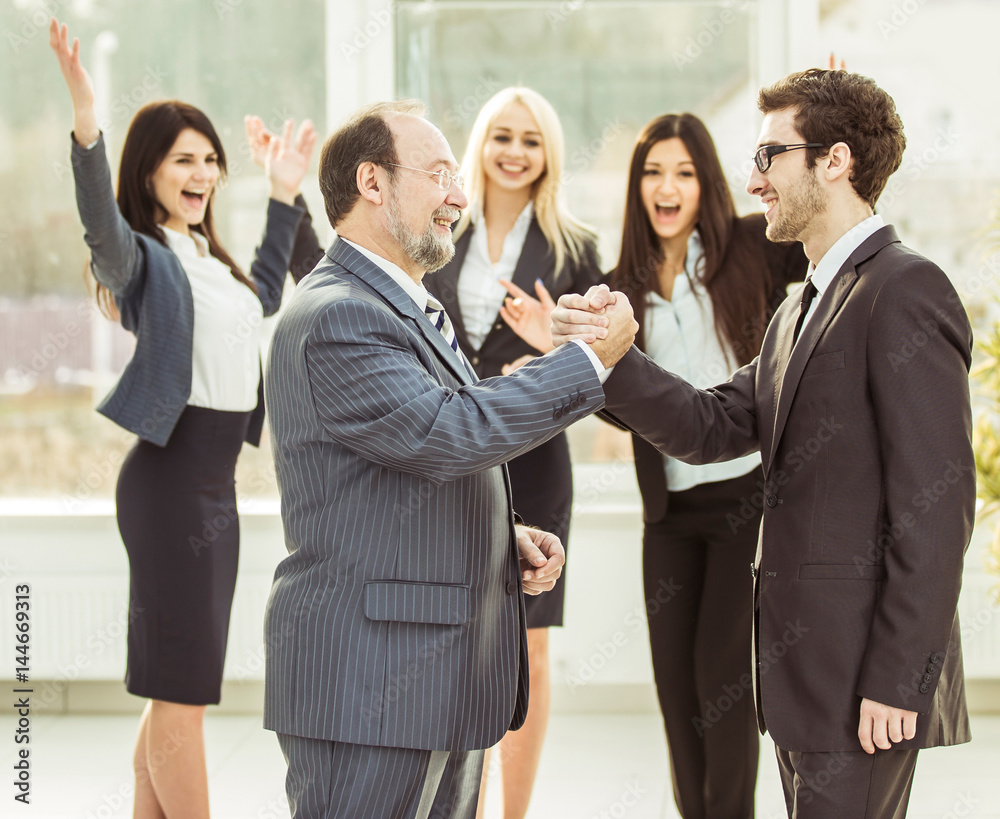 handshake of business partners on background of cheering business team handshake of business partners on background of cheering business team