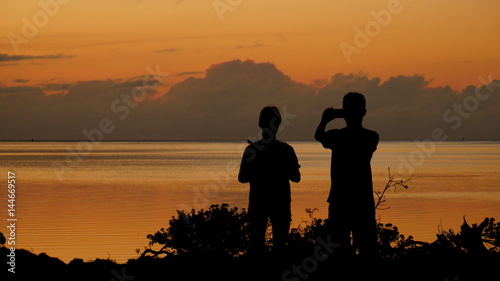 silhouette of people taking photos of the sunset Taking photos of sunsets is a favorite among many, especially in the tropical islands.