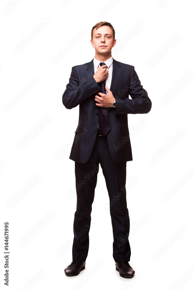 Stylish young man in suit and tie. Business style. Handsome man is standing, looking at the camera and fixing his tie Stylish young man in suit and tie. Business style. Handsome man is standing, looking at the camera and fixing his tie