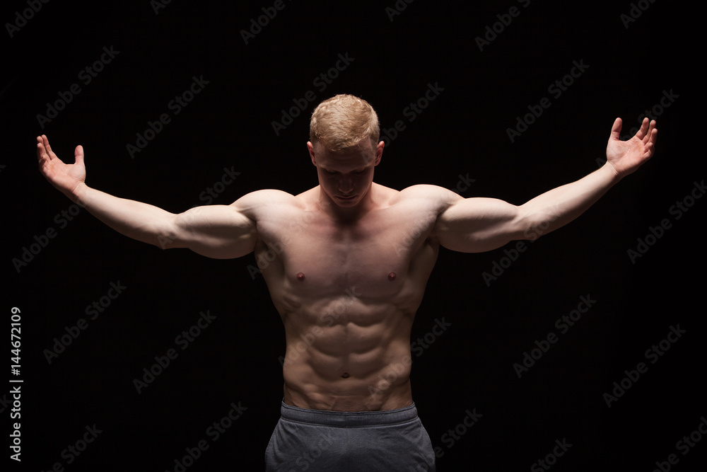 Athletic handsome man fitness-model is showing six pack abs. isolated on black background with copyspace