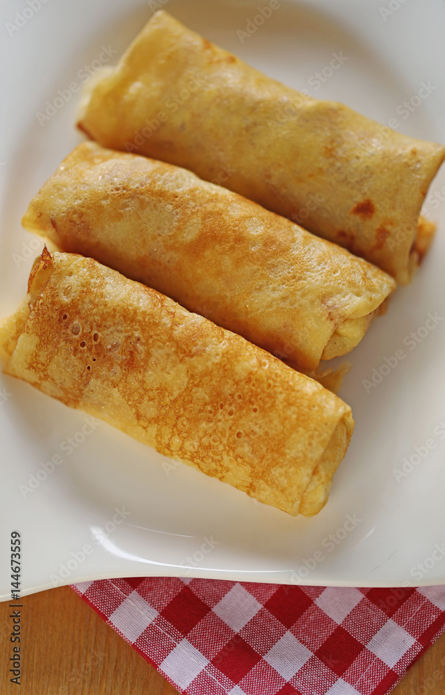 Three Stuffed pancakes on a white rectangular plate On a checkered red white napkin Three Stuffed pancakes on a white rectangular plate On a checkered red white napkin