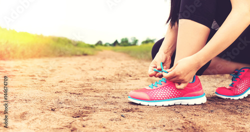 Female runner tying her running shoes on a sandy trail