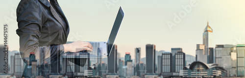 Businesswoman typing on laptop computer double exposure with blur cityscape building in morning,Business banner size,Technology communication concept